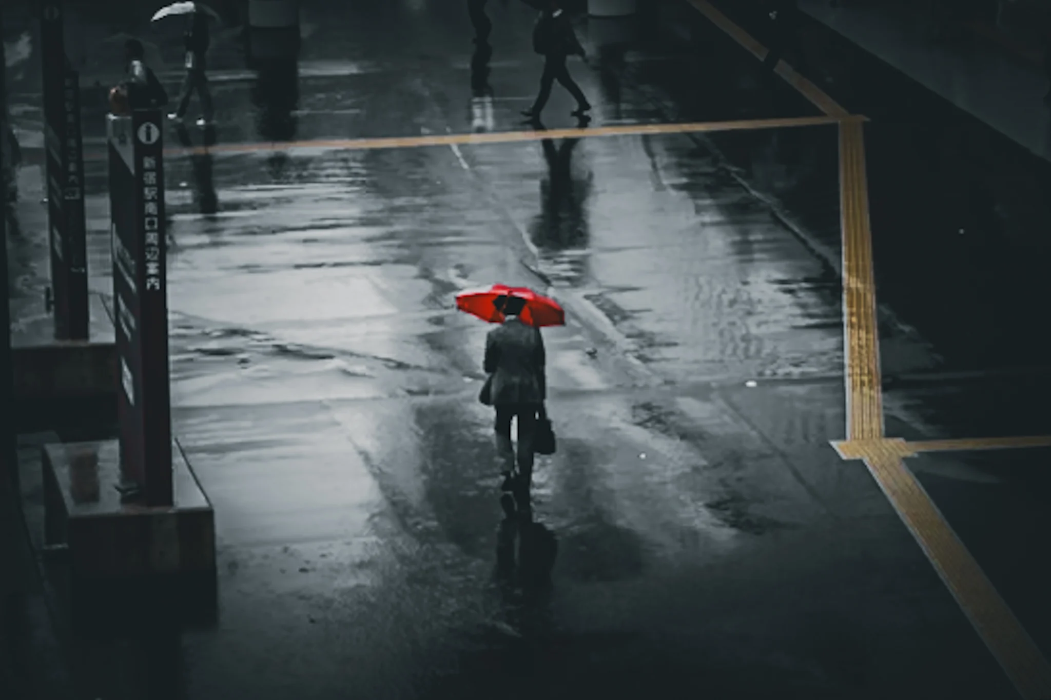 雨に濡れた街路を赤い傘で歩く人